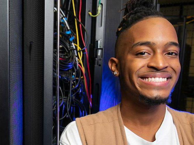 Man smiling for picture standing infront of a control panel with wires coming out of it